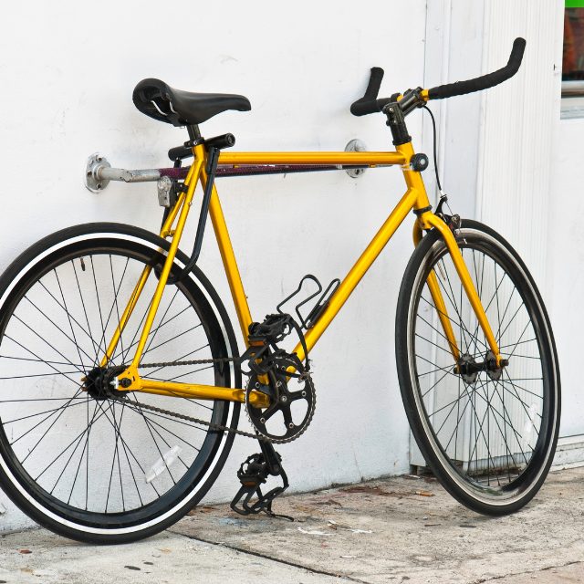 a yellow bicycle resting on a bike stand in front of a white wall