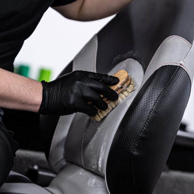 a man with black gloves scrubbing the seats of a boat with a soft-bristled brush