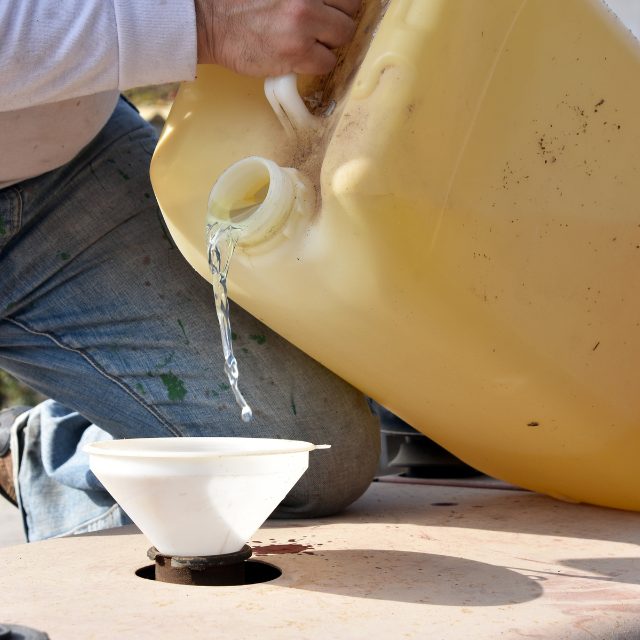 a man pouring stabiliser in a yellow fuel tank into the boat's engine with a funnel